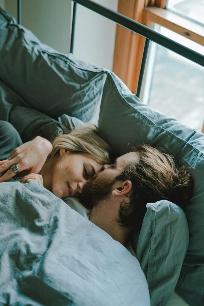 A couple lies in bed with the man giving the woman a kiss on her forehead